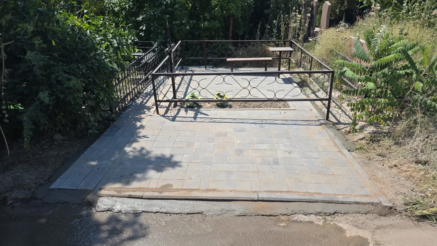Благоустройство могилы в Алматы под ключ: серая тротуарная плитка на всю площадь участка, кованая оградка, столик и лавочка, цветник